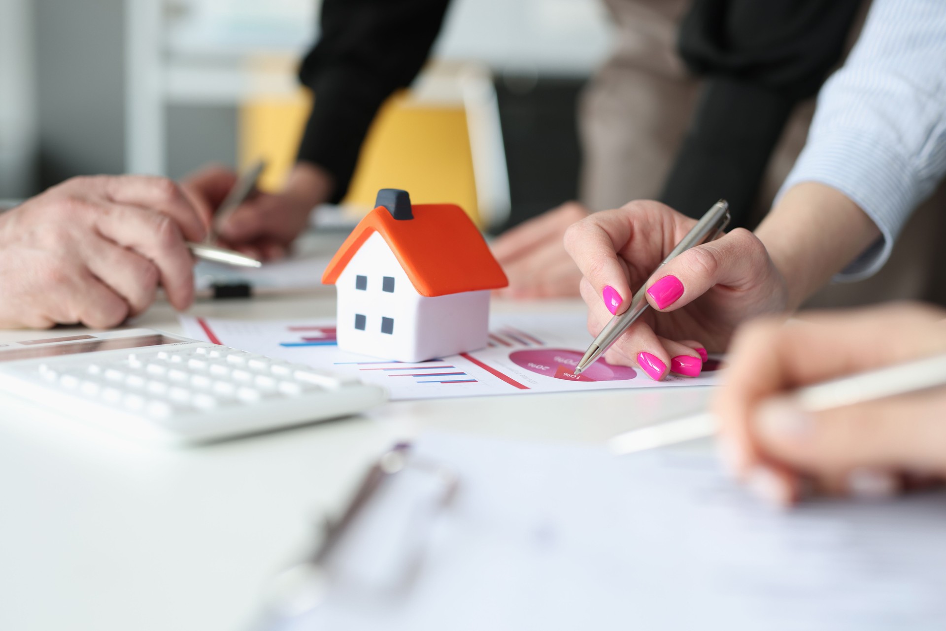 Hands of employees with pens and business charts and small house on table